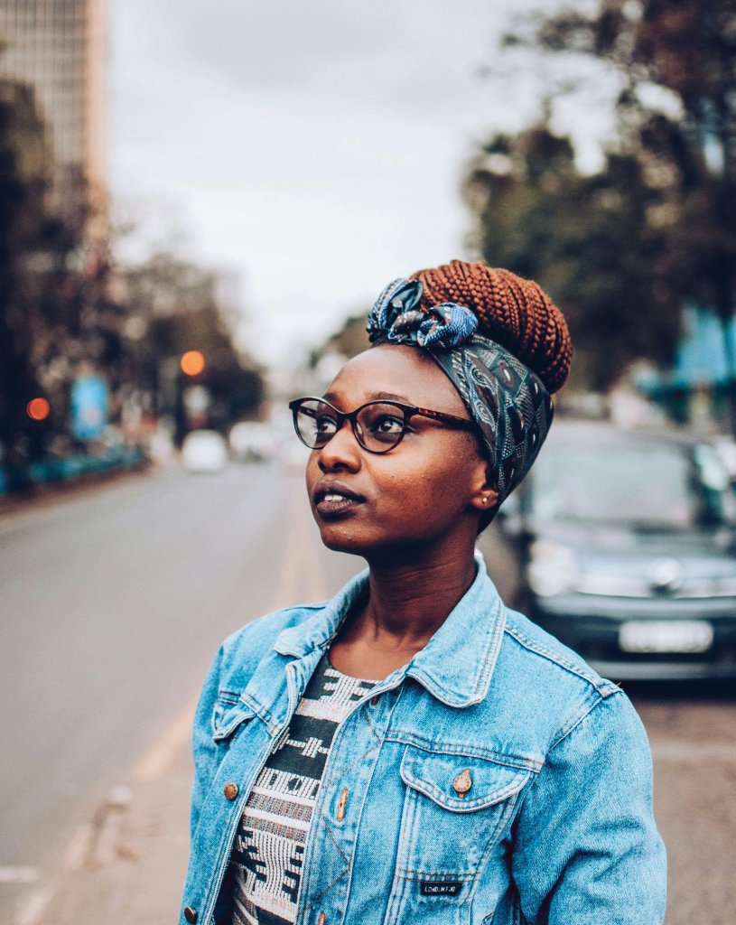Fashionable woman with headscarf and eyeglasses in city setting.