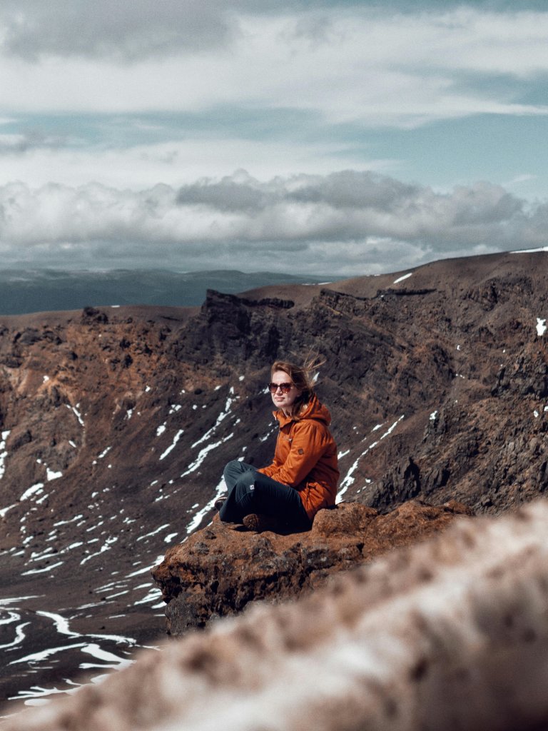 A woman sits on a cliff edge, taking in the breathtaking mountain landscape of New Zealand.