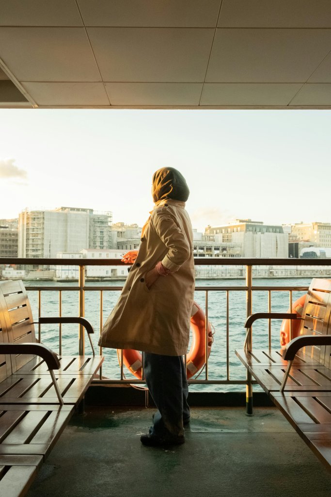 Side view of unrecognizable female passenger standing on floating ferry boat near railing fence with lifebuoy and admiring picturesque view of pier